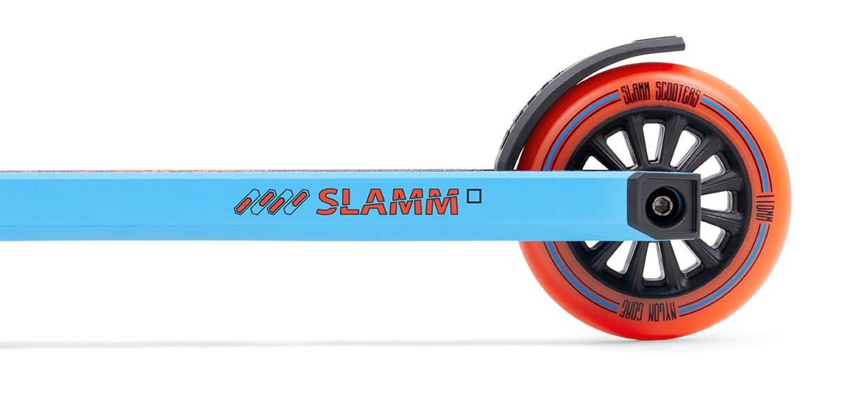 A close-up of the rear wheel on the Slamm Classic Mini Complete Stunt Scooter highlights its bright red-orange rim and black spokes. The scooter's blue metal frame features "SLAMM" in bold red lettering, making it an ideal choice for beginners in freestyle scootering.