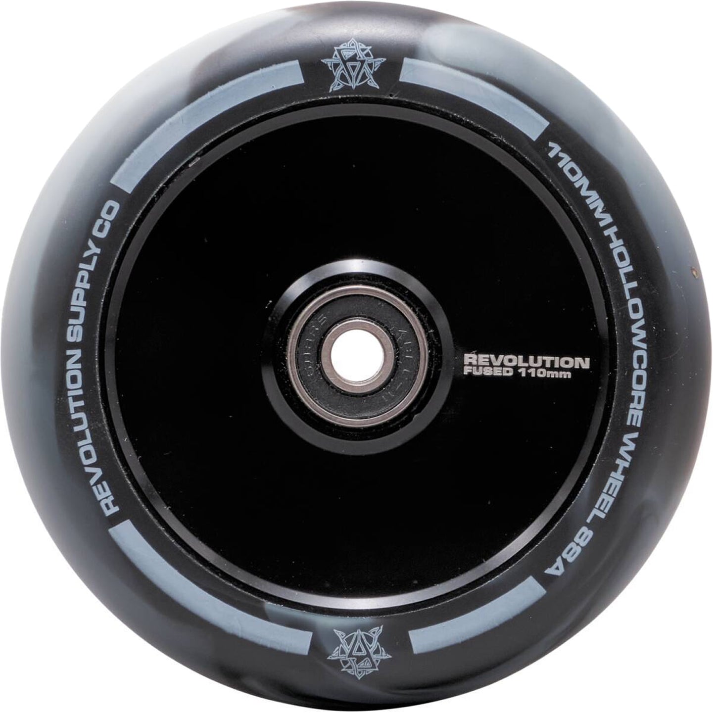 A close-up image showcases the wheel of a Revolution Fused Core 110mm Stunt Scooter, featuring "Revolution" branding on the black and white surface. Highlighting its PU development and reflective finish, the design incorporates a circular metal hub in the center, exemplifying advanced Fused Wheel Technology.