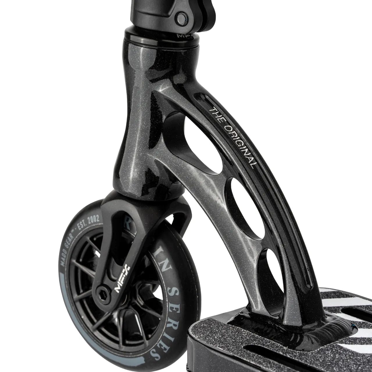 A detailed view of the Madd Gear MGP VX Origin Team Edition Complete Stunt Scooter - Chrome Black highlights its sleek, lightweight design with cutout details. The black wheel is marked with "EST. 2022," and the durable performance fork prominently features "THE ORIGINAL.