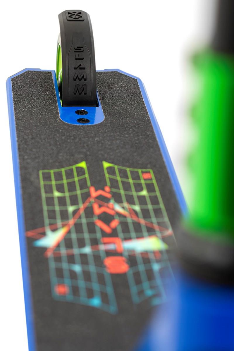 Close-up of the Slamm Classic Complete Stunt Scooter, showcasing its deck adorned with a black grip surface and a vibrant geometric design. Prominent in the image is the rear wheel with 110mm alloy construction, alongside a glimpse of the green handlebar. The scooter's primary color scheme highlights blue and green tones, reflecting its dynamic style.