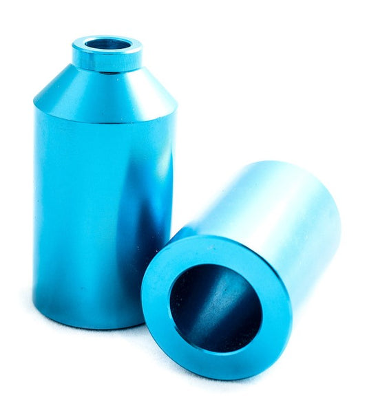 Two metallic, teal anodized cylindrical objects crafted from lightweight 6061 aluminum, with hollow centers. Labeled as Blunt Envy Aluminium Stunt Scooter Pegs, one cylinder stands upright while the other rests on its side. Both feature a conical top section leading to a smaller circular opening, ideal for stunt scooters.