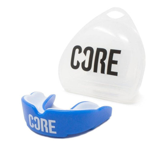 A blue and white gum shield known as the "CORE Skate Protection Mouthguard - Blue" from CORE is made with impact-absorbing materials and displayed in front of a transparent triangular case, which is also branded with "CORE".