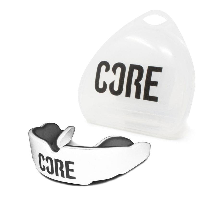 The CORE Skate Protection Mouthguard - White, featuring a white and black design with "CORE" prominently displayed on it, is showcased alongside a semi-transparent storage case that also bears the "CORE" branding. Made from impact-absorbing materials, this mouthguard includes a convenient upright case with a small handle at the top for easy carrying.