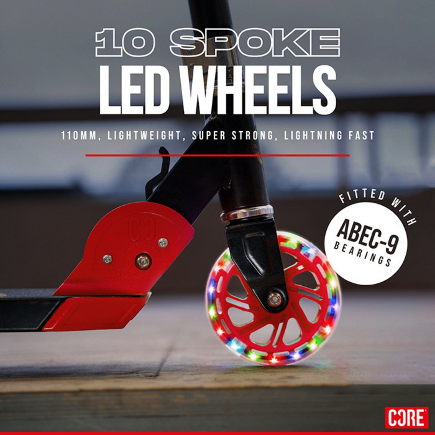 Close-up of the LED wheel on the CORE Foldy Kids LED Foldable Scooter, radiating with multicolored lights. The 10-spoke design complements a red frame. Features include: 110mm size, lightweight, strong, fast, equipped with ABEC-9 bearings. CORE branding is visible at the bottom.