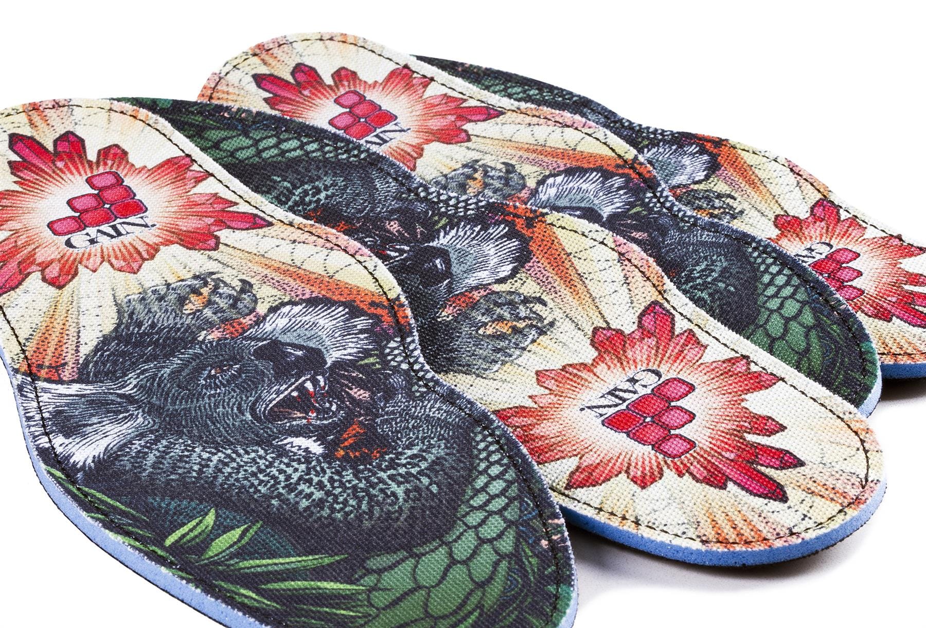 The GAIN Protection SoleBros Insoles - Dropbear, created by GAIN, offer vibrant and shock-absorbing features with a colorful illustration of a winged koala. Ideal for freestyle scooter riders, these insoles also display red sunburst patterns and a geometric logo featuring the letters "CA.M" in the center, combining style with efficient energy absorption.