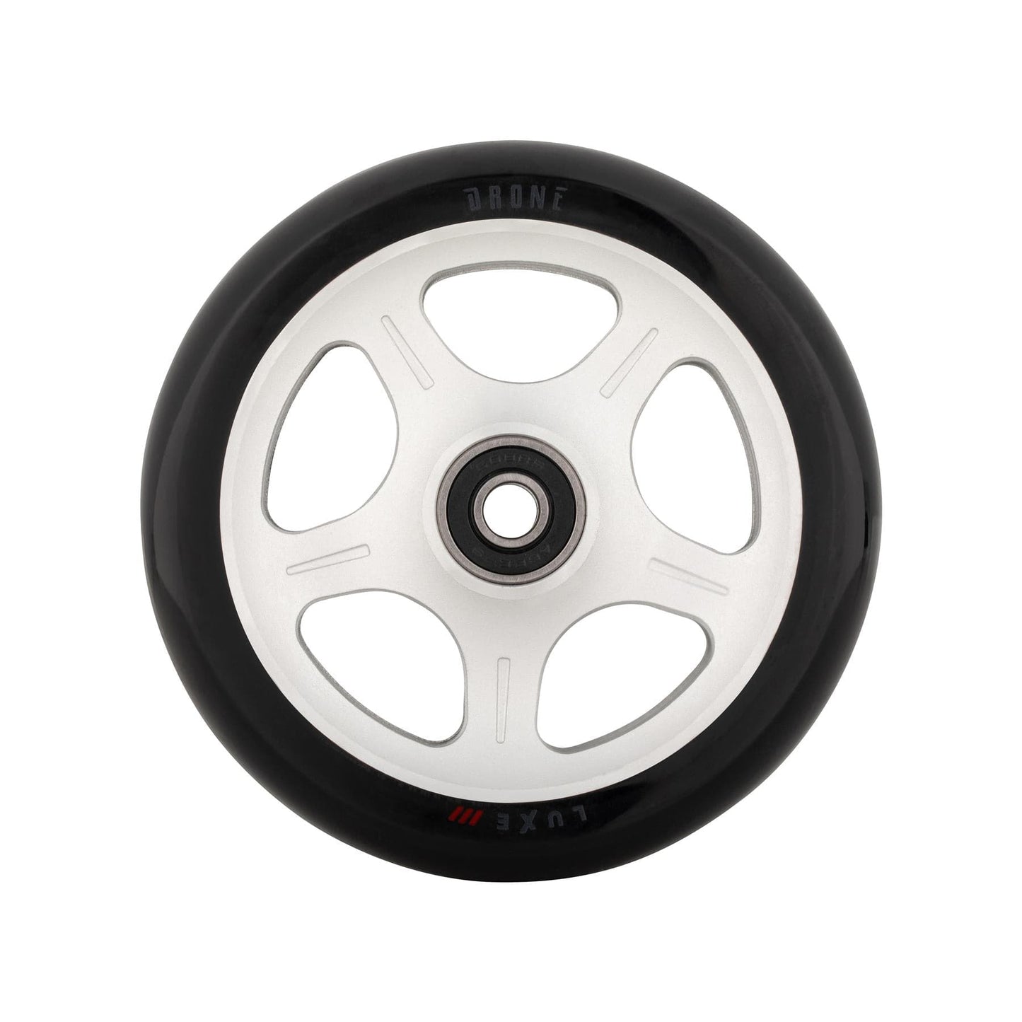 A close-up of a Drone Luxe 3 Dual-Core 110mm stunt scooter wheel reveals a black tire with a white, star-patterned core featuring five circular cutouts. "DRONE" and "Luxe" are engraved on the rim. The wheel is perfectly centered against a pristine white background.