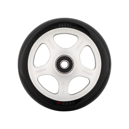 A close-up of a Drone Luxe 3 Dual-Core 110mm stunt scooter wheel reveals a black tire with a white, star-patterned core featuring five circular cutouts. "DRONE" and "Luxe" are engraved on the rim. The wheel is perfectly centered against a pristine white background.