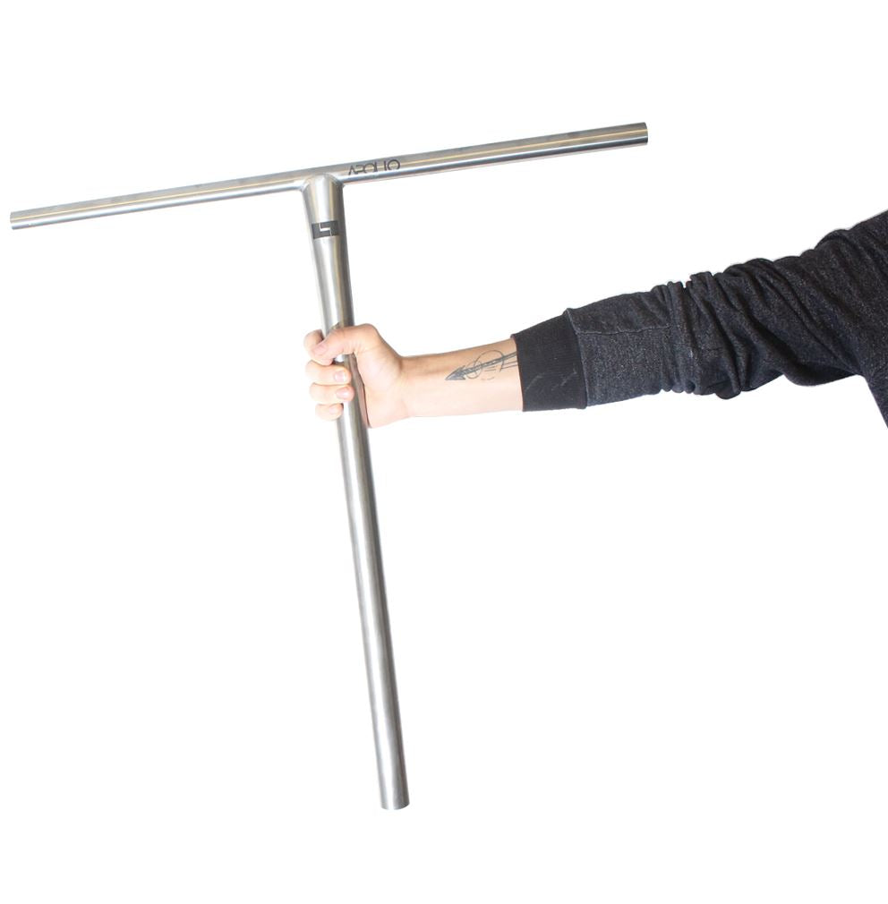 A person in a black sweatshirt holds the sleek and lightweight Logic Apollo Titanium V2 Oversized SCS Stunt Scooter Bars. Their arm extends against a plain white background, showcasing a tattoo on their forearm.