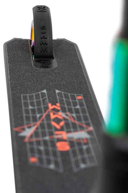 Close-up of the Slamm Classic Complete Stunt Scooter - Neochrome deck, featuring 110mm alloy wheels and a rear wheel. The deck showcases a graphic with geometric shapes and the word "Waves" in red. The black tire displays logo markings, while the scooter's green section is visible on the right side.