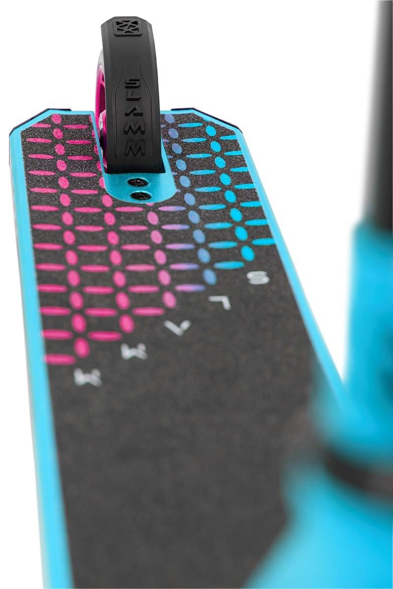 A close-up of the turquoise alloy deck on the Slamm Assault Complete Stunt Scooter - Blue showcases a multicolored dot design in shades of blue, pink, and black. At the end of the deck, a sleek 110mm aluminum wheel is prominently visible.