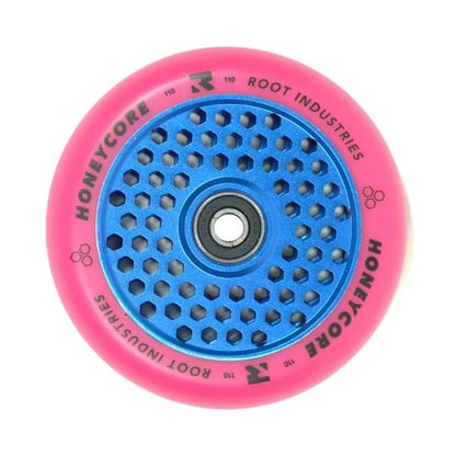 The Root Industries Honeycore 110mm Stunt Scooter Wheel in Pink and Blue features a vibrant pink design with a distinctive blue honeycomb-patterned core. It boasts Ultra High Rebound technology coupled with smooth ABEC 11 Bearings, showcasing the Root Industries branding and the word "Honeycore" elegantly printed on its surface.