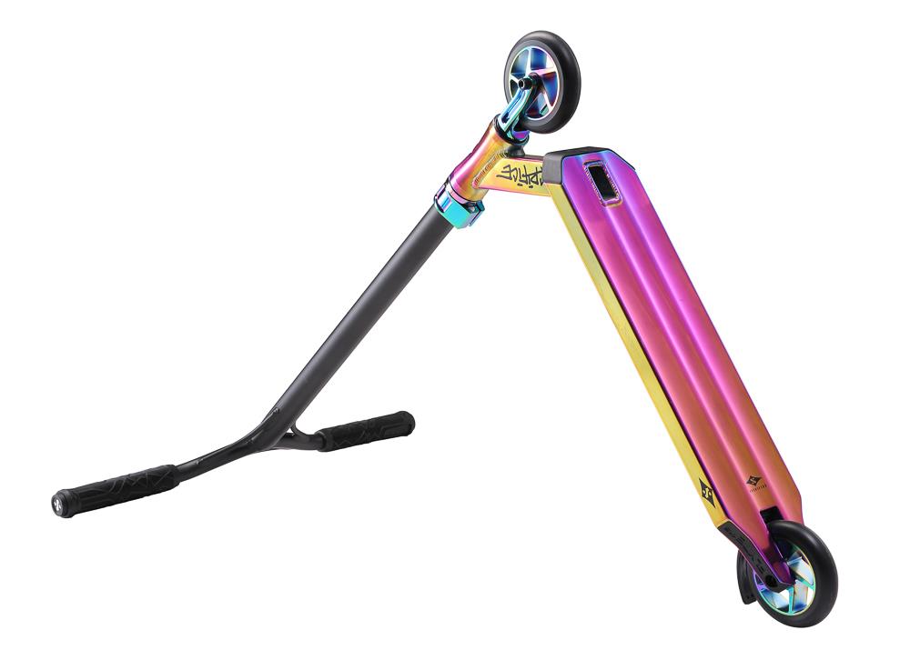 The Sacrifice Flyte 115 V2 Complete Stunt Scooter in Neochrome features a vibrant display of pink, purple, and gold hues on its iridescent deck, complemented by a black handlebar. Equipped with the IHC system and wheels that have a shiny finish, this scooter from the Sacrifice Flyte series exudes sleek design while propped up for display.