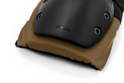 The REKD Ramp Knee Skate Protection Pads, in Black and Khaki, feature a close-up of a black pad with a brown cushion and black grommets designed for action sports. A logo adorns the impact-resistant hard shell, as the pad sits on a white surface.