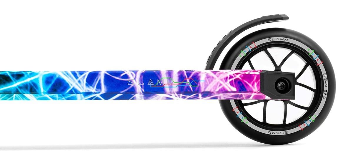 A close-up of the Slamm Strobe Complete Stunt Scooter - Multi highlights its precision engineering. The deck features a vivid blue and pink abstract design with crisscrossing lines, while the wheel is black with aluminum silver spokes, accented by striking red, green, and purple details.