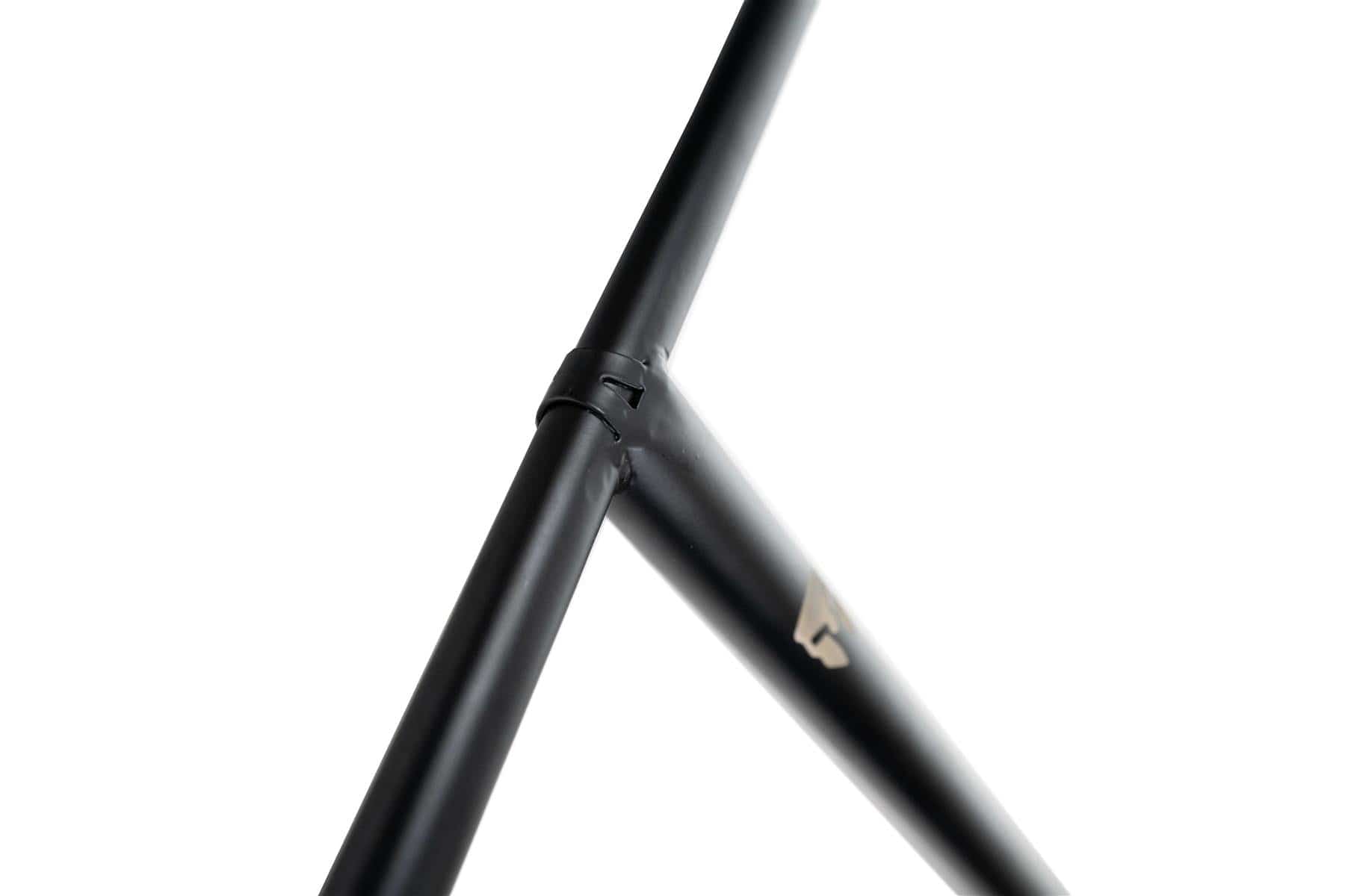 Detailed view of the junction where two Chromoly bars from the Supremacy Trojan Steel Oversized SCS Stunt Scooter T-Bars intersect, one positioned vertically and the other diagonally. This black, minimalist design by Supremacy is set against a white background, emphasizing its sleek aesthetic.