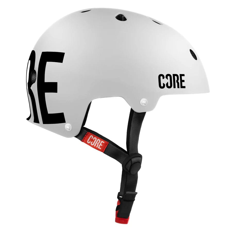 The CORE Action Sports Skate / Scooter Helmet in white features black "CORE" branding on the side, offering a blend of comfort and style. It comes equipped with a black adjustable chin strap highlighted by a red accent, along with several ventilation holes to improve breathability, making it perfect for skating.