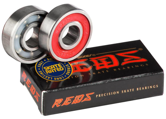 A pair of skateboard bearings with a visible red seal is next to a black and red box labeled "Bones Reds Skateboard Bearings - 2 Pack" by Bones. A nearby yellow and blue circular sticker reads "Skate Rated," highlighting the trusted quality for exceptional skate performance.