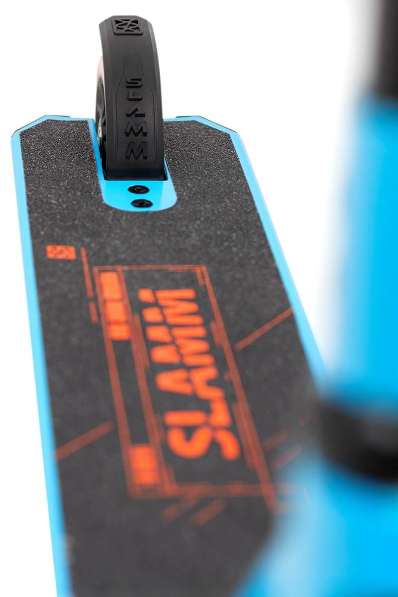 Close-up of the Slamm Classic Mini Complete Stunt Scooter - Blue, showcasing a black grip tape adorned with orange "SLAMM" graphics. The rear wheel, partly concealed by the deck, displays the word "SLAMM" embossed on the tire—an ideal choice for beginners in freestyle scootering.