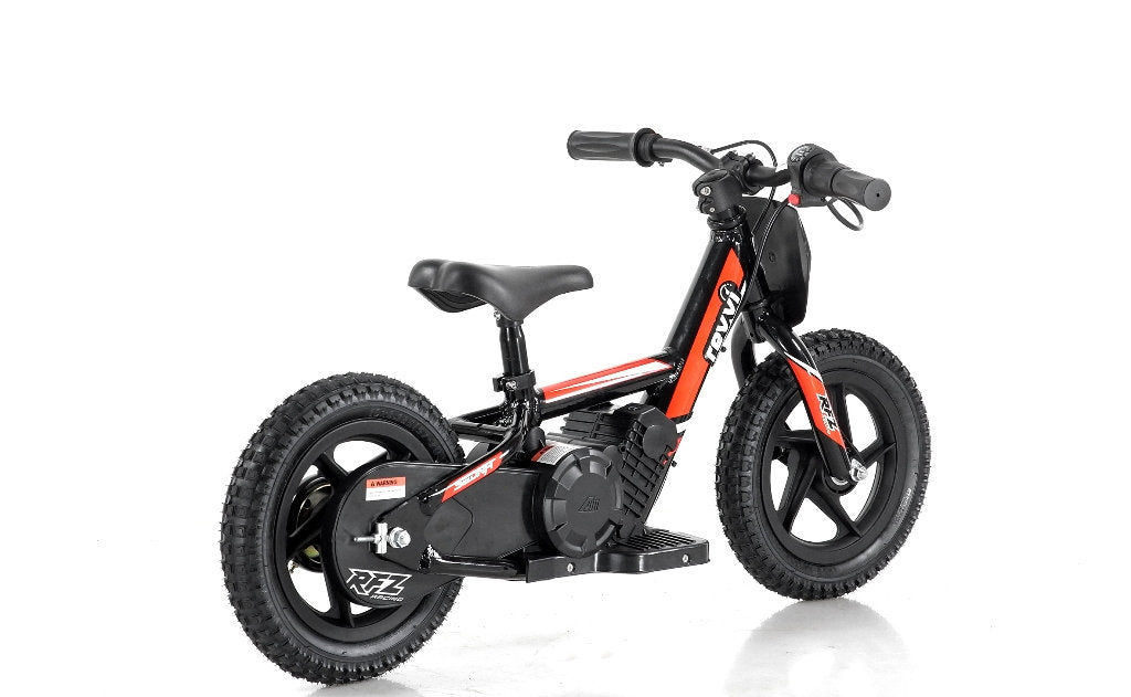 A side view of the Revvi 12" Kids Electric Balance Bike - Red is displayed against a plain white background, showcasing its small size and sturdy frame in black and red. With thick tires and no pedals, this bike from Revvi is designed perfectly for kids learning balance and progression.