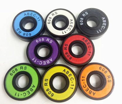 Presenting the Skates.co.uk ABEC 11 Candy Skateboard Bearings - 8 Pack, a lively assortment of skateboard bearings available in a spectrum of colors including blue, black, white, purple, orange, red, yellow, and green. Each bearing is intricately labeled with "ABEC-11" and "608 RS," beautifully displayed in a circular arrangement.