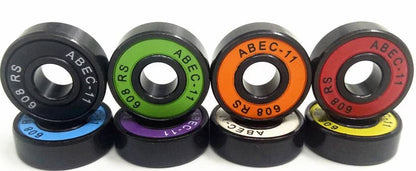 A set of six Skates.co.uk ABEC 11 Candy Skateboard Bearings is artfully arranged, each bearing featuring a sleek black exterior with a colorful center in hues of lime green, purple, green, orange, black, and yellow. Labeled with "ABEC-11 608 RS," they are neatly stacked for display.