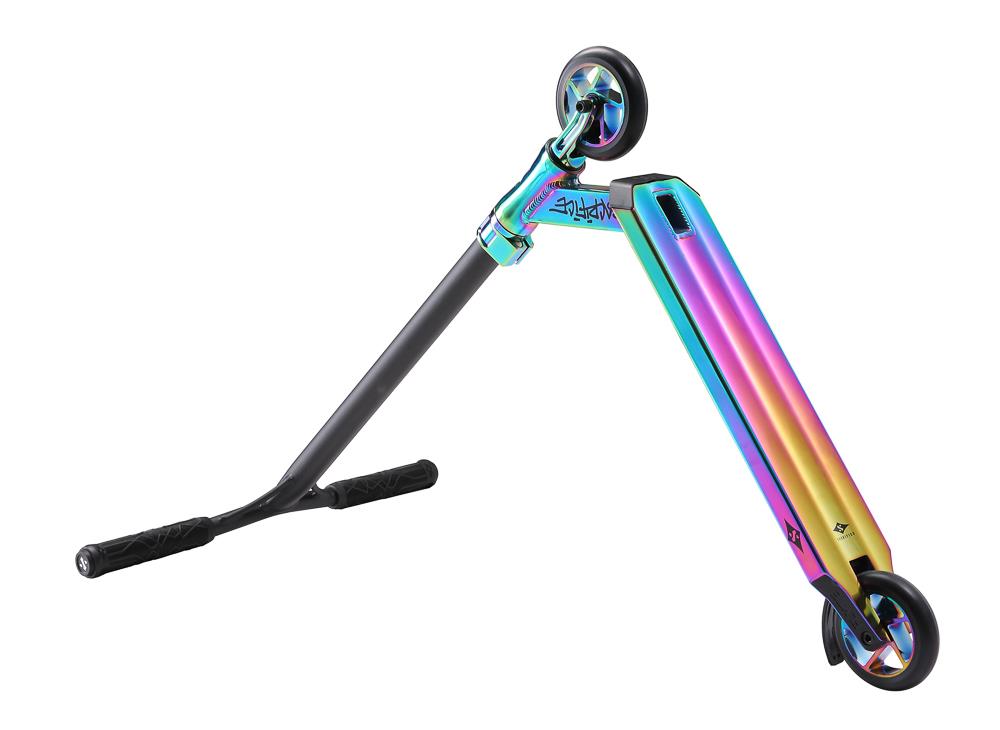 The Sacrifice Flyte 100 V2 Complete Stunt Scooter in Neochrome features a lightweight, multicolored design with a metallic rainbow finish on the deck. It is equipped with black handles and two wheels of different sizes—a smaller one at the front and a larger one at the rear. The scooter is angled and resting on its side.