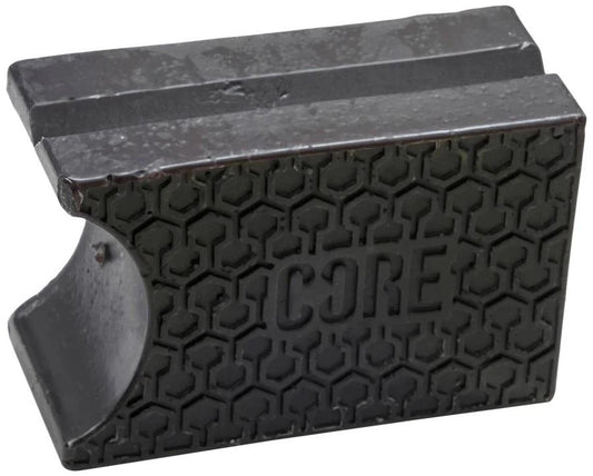 A liquorice black metal object featuring a hexagonal pattern on its surface and the "CORE" logo embossed in the center resembles pre-grooved shapes. The piece has a grooved top edge and a smooth, curved side, exuding an industrial look similar to CORE Epic Skate Wax.