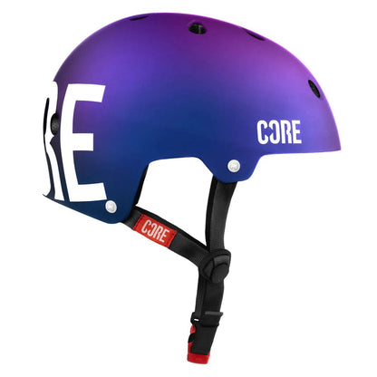 A side view of the CORE Street Skate/Scooter Helmet in a neo and white color gradient displays the brand name "CORE" prominently in large white letters on the side. This helmet is designed for street use and includes ventilation holes, along with an adjustable black strap featuring a red label that also reads "CORE.