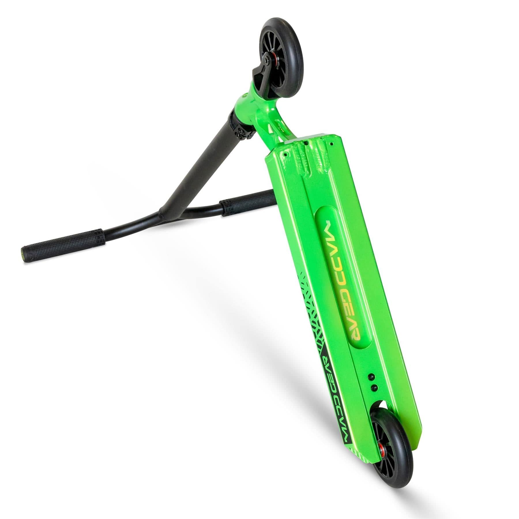 A Madd Gear (MGP) VX Origin III 450 Stunt Scooter in Dragon Skin is propped up, highlighting its design: sleek black aluminium handlebars with textured grips, a striking green deck with a logo, and contrasting black wheels.