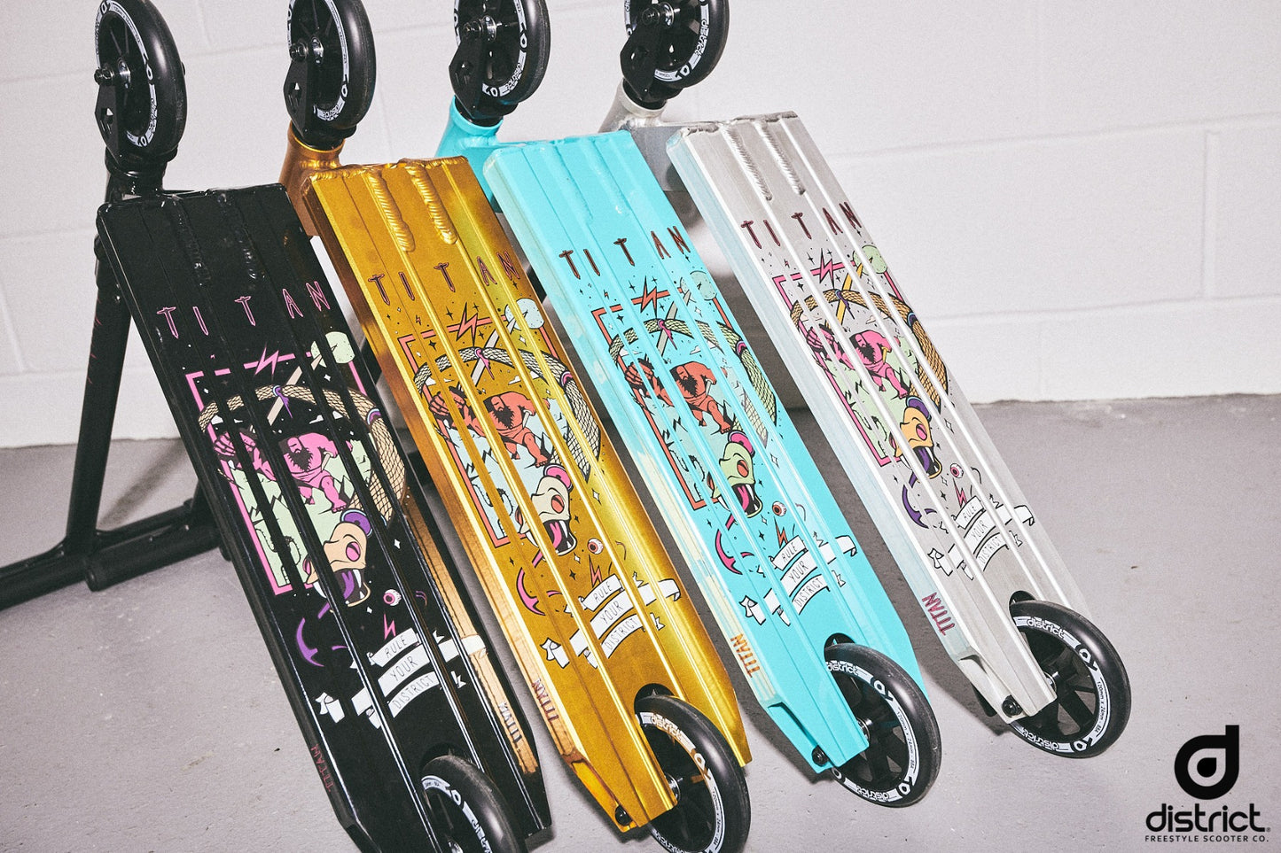 Five vibrant stunt scooters with intricate graphic designs are displayed leaning against a white wall, resembling the colorful skateboards popular among pro-level riders. These scooters feature black decks with striking patterns, and a District logo is prominently visible at the bottom right corner, reminiscent of the District Titan Complete Stunt Scooter - Black.