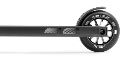 Close-up side view of the Slamm Classic Complete Stunt Scooter - Black, highlighting the rear wheel and part of the deck. The 110mm alloy wheels display the text "SLAMM SCOOTERS 110MM 88A," and the deck boasts a textured grip design.