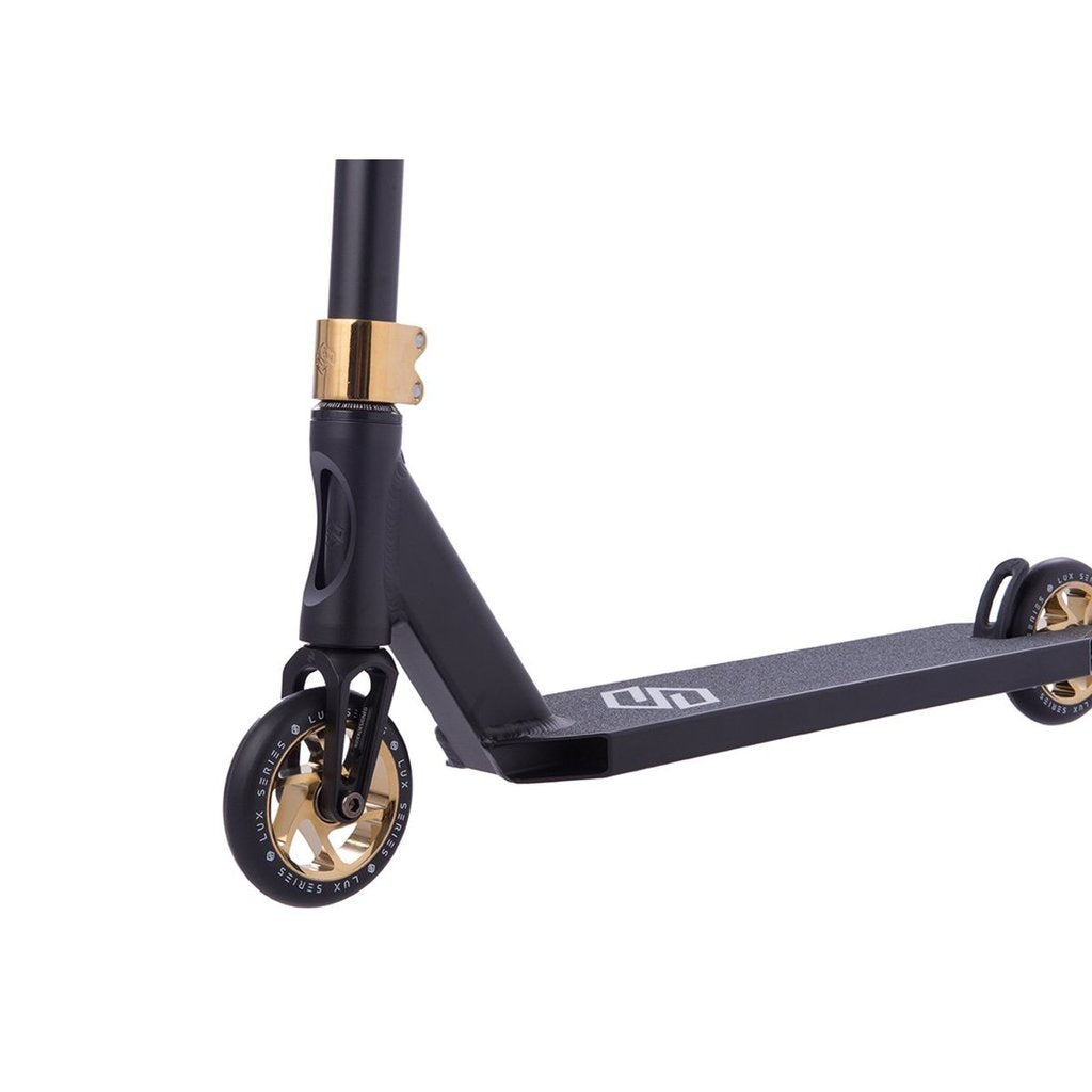 Close-up of the Striker Lux Pro Complete Stunt Scooter in gold chrome, emphasizing its lightweight aluminum frame. The front displays a gold wheel hub and clamp, complemented by black handlebars and a textured deck featuring the brand logo. Set against a plain white background, it exudes sleek sophistication.