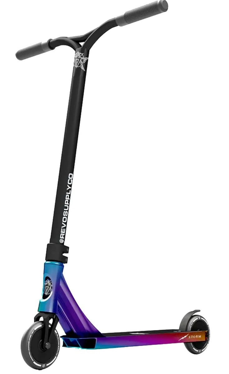 The Revolution Storm Complete Stunt Scooter - Neochrome showcases vibrant hollow core wheels and a sleek black handlebar. The storm deck exhibits a captivating gradient that smoothly transitions from blue to purple to red, with the brand name "Revolution" prominently featured on both the handlebar and deck.