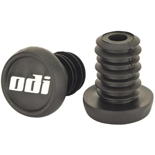 The image depicts two black handlebar grips with "odi" inscribed on them. One grip is positioned upright to display its ridged design, secured with ODI Push-In Stunt Scooter Bar Ends for a reliable fit, while the other rests horizontally, highlighting both the flat end and options for color customization.