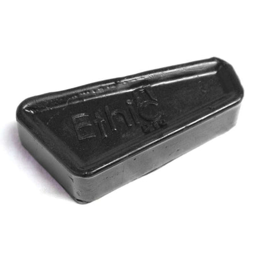 A black, wedge-shaped piece of Ethic DTC Stunt Scooter Wax features the word "Ethic" embossed on its surface, making it ideal for enhancing grinds and slides. Its smooth finish is suitable for skateboard decks, ledges, and rails. The wax is elegantly showcased against a plain white background.