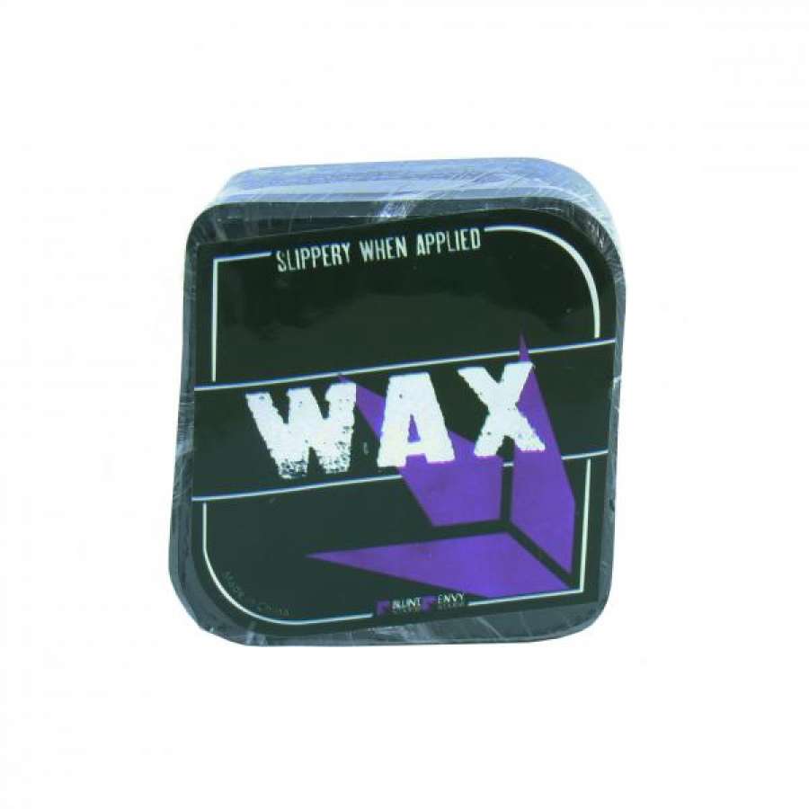 The Blunt Envy Stunt Scooter Wax - Black comes in a black square container with "WAX" printed prominently in bold white letters and "SLIPPERY WHEN APPLIED" at the top. The packaging is enhanced with a purple geometric design, making it perfect for handling the most challenging ledges and rails. The product is wrapped in plastic for protection.