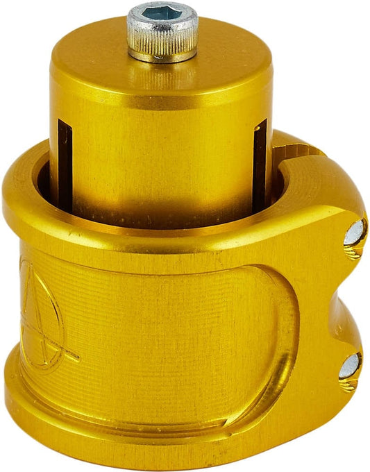 Close-up of a shiny, gold-colored mechanical part with a cylindrical shape, featuring bolts and grooves. The design is complemented by an engraved geometric logo or pattern on its surface, resembling the sleek Apex Lite 2 Bolt Oversized Stunt Scooter Clamp & HIC Kit by Apex.