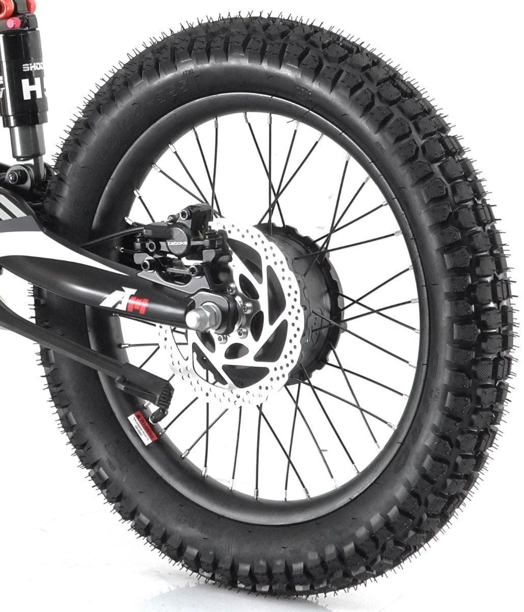 A close-up of the rear wheel on the Revvi 18" Kids Electric Balance Bike, featuring a knobby tire and equipped with a disc brake system and shock absorber, highlights its off-road capability. This striking red bike is perfect for young adventurers craving both style and performance on rugged terrain.