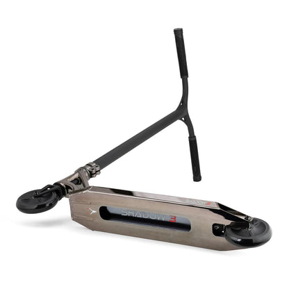 A stylish kick scooter in smoked chrome, featuring the Helios Hollow-Spoked Wheels and a flat deck with the "Drone Shadow 3 Feather-Light Complete Stunt Scooter" branding. The T-shaped handlebar is adorned with comfortable black grips, and the scooter is showcased beautifully on a white surface.