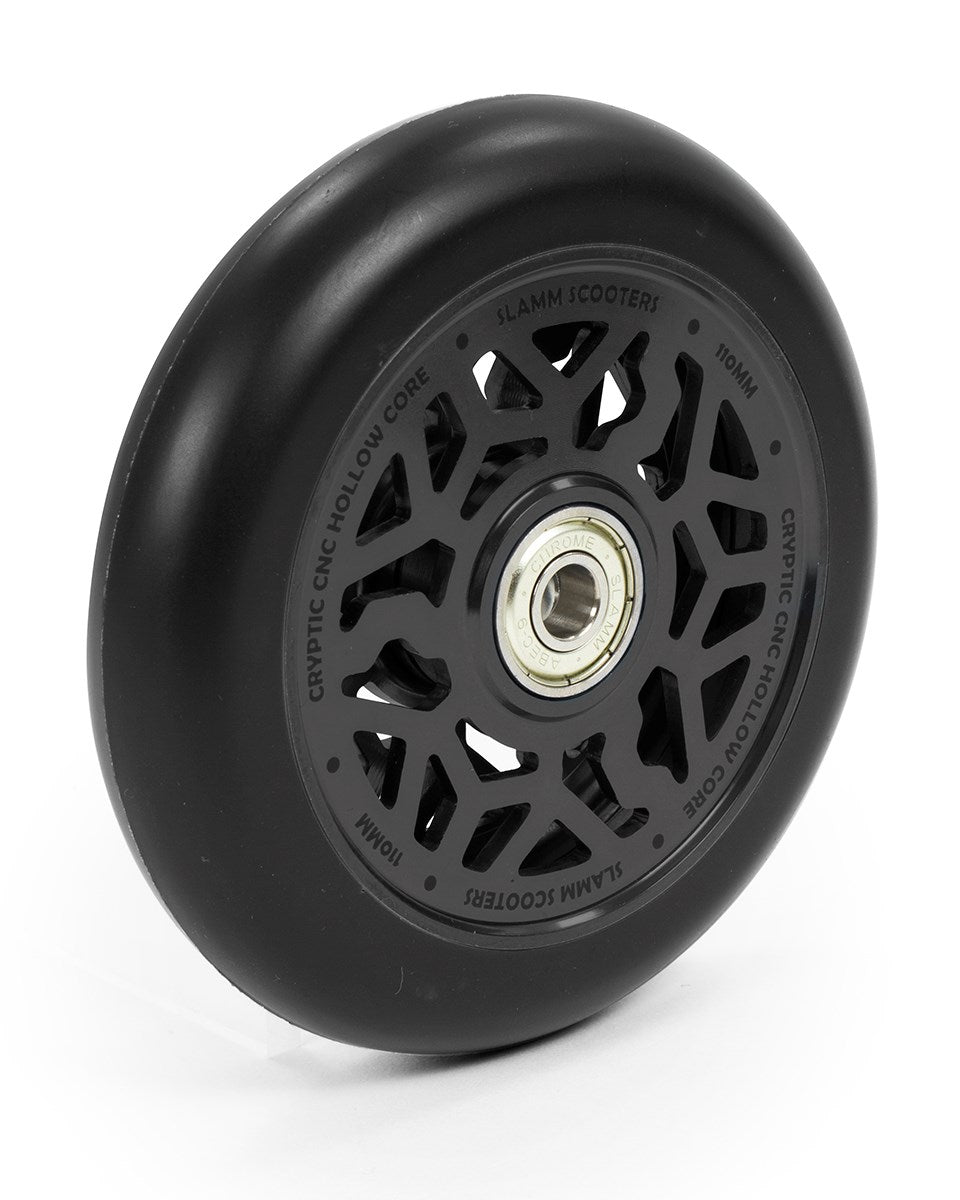 The Slamm Cryptic 110mm Stunt Scooter Wheel - Black boasts a sophisticated black appearance with geometric cutouts and exposed ABEC-9 chrome bearings. The hollow core is engineered for superior performance, labeled around the perimeter, and constructed from Super High Rebound Mi-T Urethane to ensure an exceptionally smooth ride.