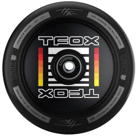 The Lucky Tanner Fox TFox Signature 110mm Stunt Scooter Wheel in black prominently displays "TFOX" on both sides of its central hub. This circular design features "LUCKYSPEED" and utilizes high-rebound PU. The rim is inscribed with the phrase "ONE HUNDRED TEN MILLIMETERS" and is equipped with Lucky ABEC 7 bearings.