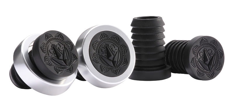 Four screw caps in black and silver are displayed, showcasing engraved geometric designs on their tops. Made using premium thermoplastic rubber compounds, two are shown upright while the other two are tilted to reveal the spiral threading beneath.